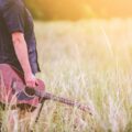 man carrying brown cutaway acoustic guitar standing on green grass field